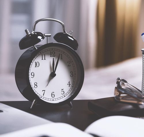 Reloj analógico junto a un bote de bolígrafos y un ordenador portátil.