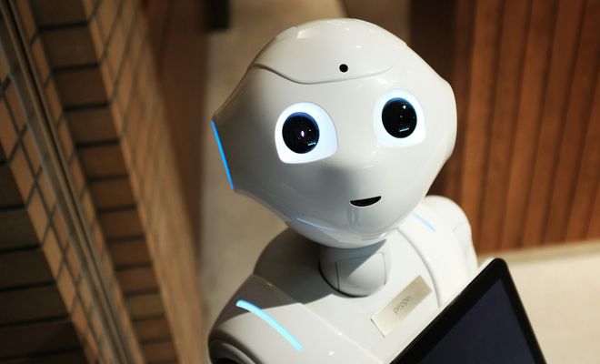 Primer plano de un robot Pepper blanco con ojos azules brillantes y una sonrisa sutil, sujetando una tablet negra.
