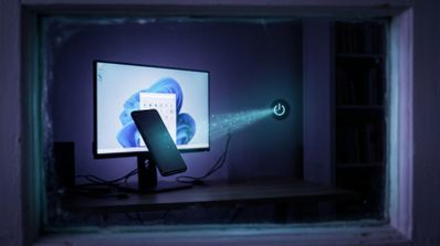 Un teléfono móvil levita frente a un monitor con Windows 11 mientras un haz de luz con código binario se dirige hacia un icono flotante de apagado.