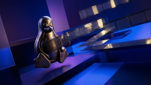 Figura metálica del pingüino Tux sobre un fondo azul con cintas de película cinematográfica flotando a su alrededor.