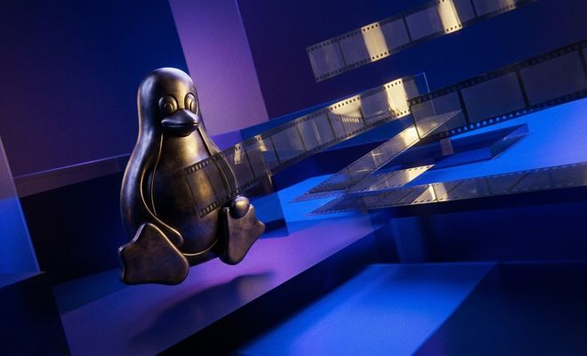 Figura metálica del pingüino Tux sobre un fondo azul con cintas de película cinematográfica flotando a su alrededor.