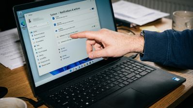Primer plano de una mano señalando el menú de configuración de notificaciones en la pantalla de un ordenador portátil con Windows 11.