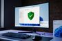 Monitor de ordenador mostrando la interfaz de Seguridad de Windows con un escudo verde de verificación sobre un escritorio con teclado y ratón.