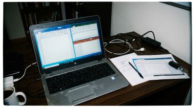 Ordenador portátil sobre un escritorio mostrando aplicaciones de Microsoft Office divididas en pantalla junto a notas físicas.