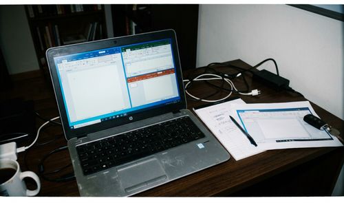 Ordenador portátil sobre un escritorio mostrando aplicaciones de Microsoft Office divididas en pantalla junto a notas físicas.