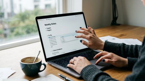 Persona utilizando la interfaz de Notion en un portátil para organizar una lista de tareas y una base de datos de clientes.