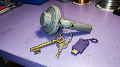 Conjunto de llaves físicas tradicionales y una llave de seguridad USB junto a un dial de caja fuerte metálico sobre una mesa de trabajo.
