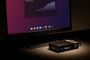 Monitor que muestra la interfaz de Raspberry Pi OS con un nuevo dock inferior de aplicaciones junto a una placa Raspberry Pi en su carcasa.