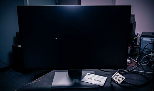 Monitor de ordenador encendido con la pantalla completamente negra y solo el cursor del ratón visible sobre una mesa de trabajo.