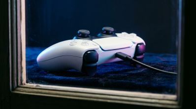 Mando DualSense blanco conectado por cable USB sobre una superficie oscura con iluminación azul y violeta.
