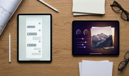 Dos tabletas sobre una mesa de madera, una mostrando una interfaz de chat y la otra controles de edición de imagen sobre una fotografía de montañas.
