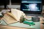 Libro abierto junto a un candado y una flecha con luces LED verdes en una mesa de trabajo con un ordenador portátil al fondo.