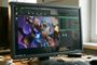 Monitor de ordenador mostrando una sesión de trabajo en Linux con una aplicación de diseño 3D y varias ventanas de terminal y gestión de archivos sobre un escritorio de madera.
