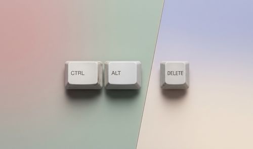 Tres teclas blancas de un teclado clásico con las etiquetas CTRL, ALT y DELETE dispuestas horizontalmente sobre un fondo de tonos pastel.