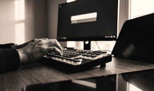 Manos de una persona utilizando un teclado mecánico frente a un monitor que muestra la interfaz de búsqueda de Flow Launcher en Windows.