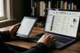 Persona utilizando el software Calibre en un ordenador portátil junto a un lector de libros electrónicos Kindle en una mesa de madera.