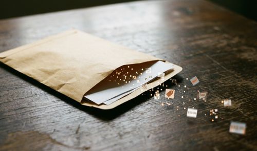Sobre de papel abierto en una mesa de madera del cual salen partículas digitales e iconos de compras y precios.