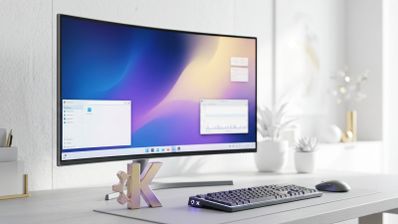 Monitor curvo que muestra el escritorio de KDE Plasma con ventanas abiertas junto al logotipo de KDE en una mesa de trabajo.