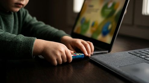 Manos de un niño conectando una memoria USB azul en el puerto lateral de un ordenador portátil con la pantalla encendida.