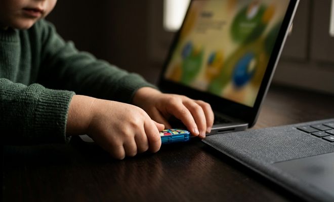 Manos de un niño conectando una memoria USB azul en el puerto lateral de un ordenador portátil con la pantalla encendida.