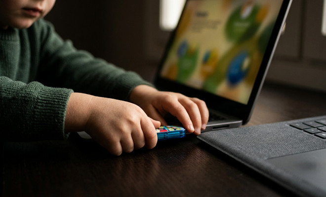 Manos de un niño conectando una memoria USB azul en el puerto lateral de un ordenador portátil con la pantalla encendida.