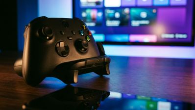 Mando inalámbrico de Xbox de color negro en primer plano sobre una mesa, con la interfaz de Windows 11 en modo juego desenfocada al fondo.