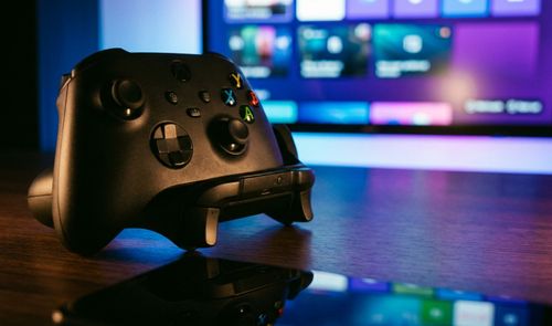 Mando inalámbrico de Xbox de color negro en primer plano sobre una mesa, con la interfaz de Windows 11 en modo juego desenfocada al fondo.