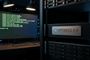 Monitor de ordenador con líneas de código y servidor en rack con placa metálica grabada con el logotipo de Puffy y el texto OpenBSD 8.0.