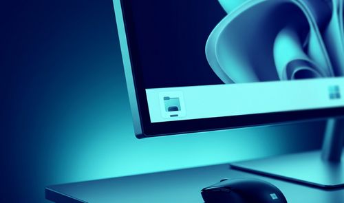 Primer plano de un monitor con la interfaz de Windows 11, mostrando el icono del Explorador de archivos en la barra de tareas sobre un escritorio iluminado en tonos azules.