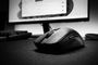 Primer plano de un ratón de ordenador negro sobre una alfombrilla frente a un monitor con Windows 11.