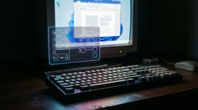 Teclado mecánico clásico en primer plano frente a un monitor con una interfaz de realidad aumentada que muestra diagramas de atajos de teclado.