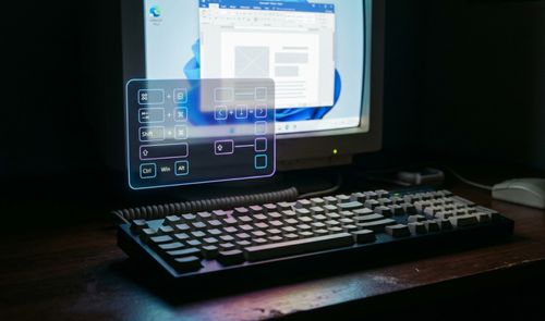 Teclado mecánico clásico en primer plano frente a un monitor con una interfaz de realidad aumentada que muestra diagramas de atajos de teclado.