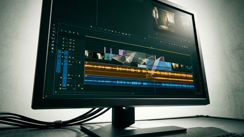 Interfaz de un editor de vídeo en un monitor de sobremesa con líneas de tiempo y ondas de audio.