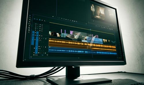 Interfaz de un editor de vídeo en un monitor de sobremesa con líneas de tiempo y ondas de audio.