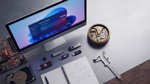 Escritorio con monitor que muestra la ventana de Windows Update junto a componentes de hardware, un reloj de engranajes y herramientas de medición.
