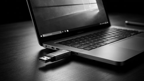Memoria USB conectada al puerto lateral de un ordenador portátil sobre una mesa oscura.