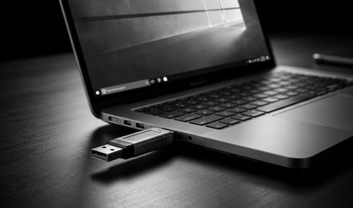 Memoria USB conectada al puerto lateral de un ordenador portátil sobre una mesa oscura.