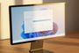 Monitor de ordenador mostrando el fondo de escritorio de Windows 11 con una ventana de progreso de actualización sobre una mesa de madera.
