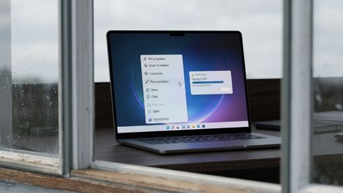 Ordenador portátil mostrando el menú contextual de Windows con opciones de personalización y una barra de progreso de descarga de 5 GB.