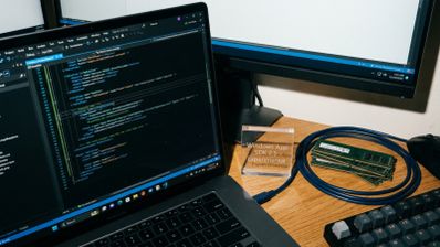 Entorno de desarrollo con código fuente en un portátil junto a varios módulos de memoria RAM sobre un escritorio.